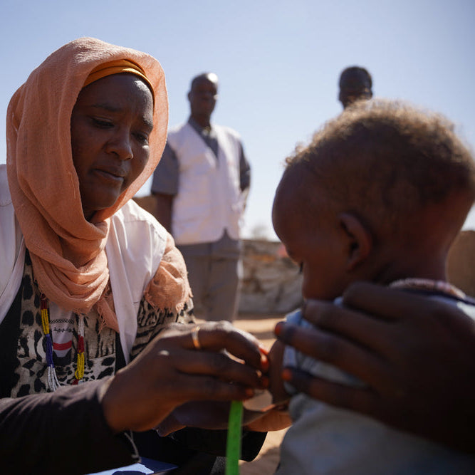Woman in a pink headscarf holding a child with a clear sky background