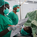 Medical professionals in green scrubs and masks in a hospital setting.