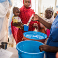 People in a community setting with blue buckets and a child being held.