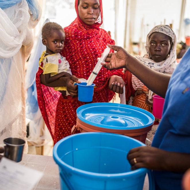 People in a community setting with blue buckets and a child being held.