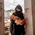 Woman holding a baby in front of a vehicle with a visible license plate.